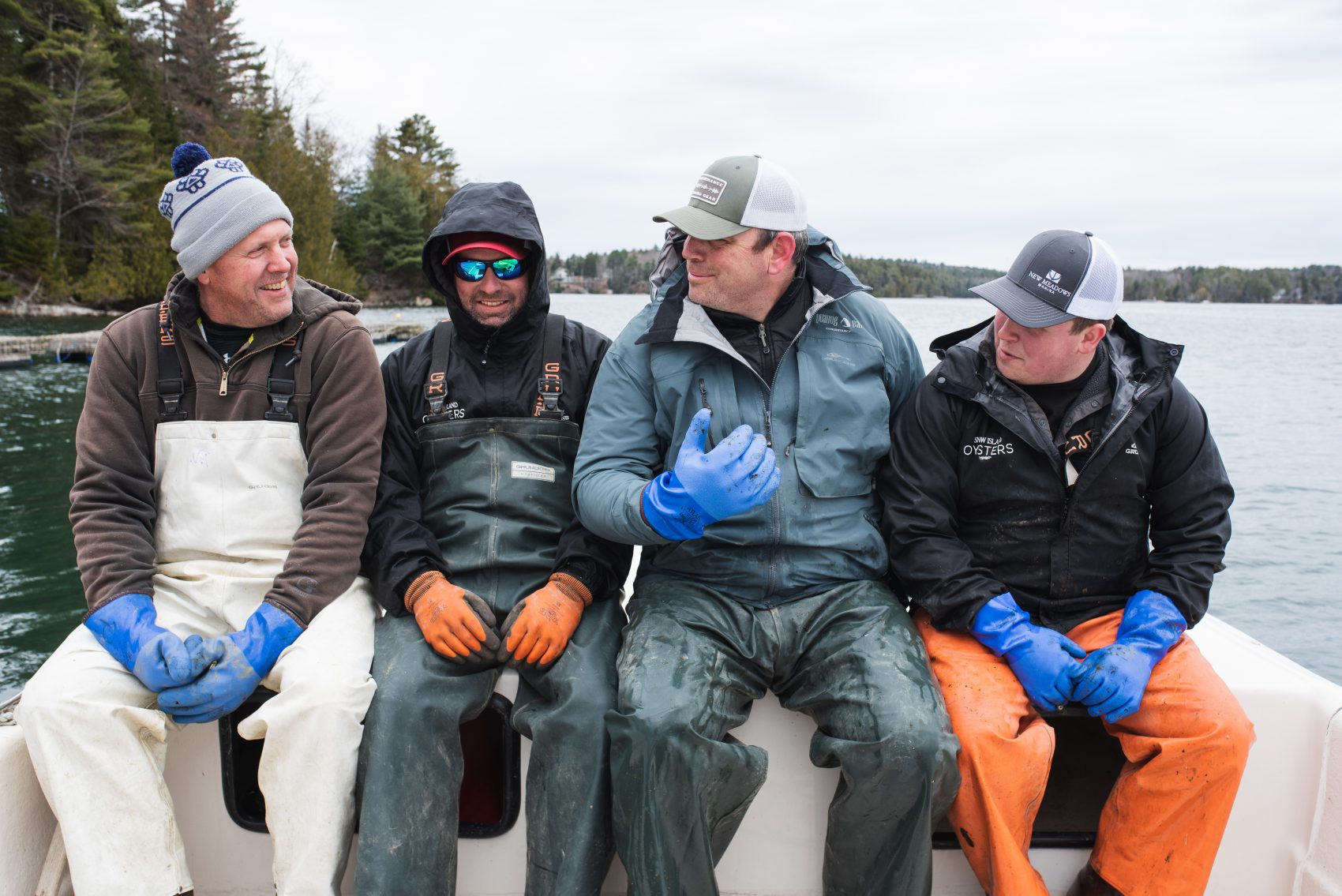 Peter, Donnie, Dave and Alec of Snow Island Oysters sit next to one another on the bow of their boat.